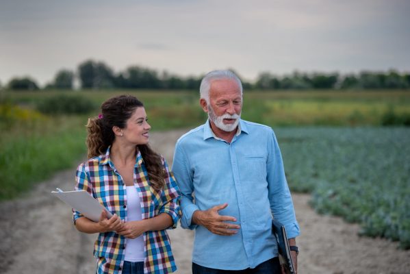 Senior farmer and smiling young woman walking on agricultural field and talking